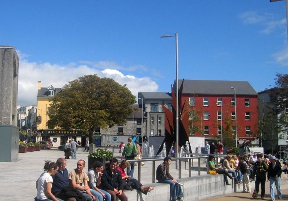 people sitting on the wall in Eyre Square on a sunny blue day