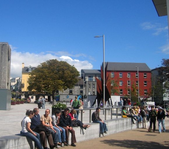 people sitting on the wall in Eyre Square on a sunny blue day