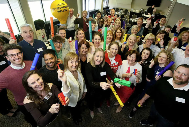 30+ smiling adults old and young holding up plastic tubes, stress balls and a xylophone.